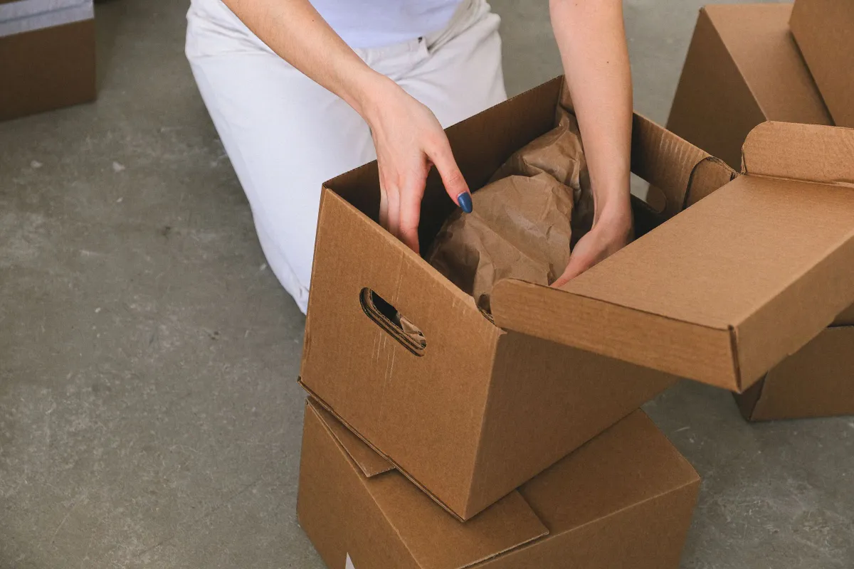 Illustrative stock photo: hands carefully packing a wrapped household item into a moving box
