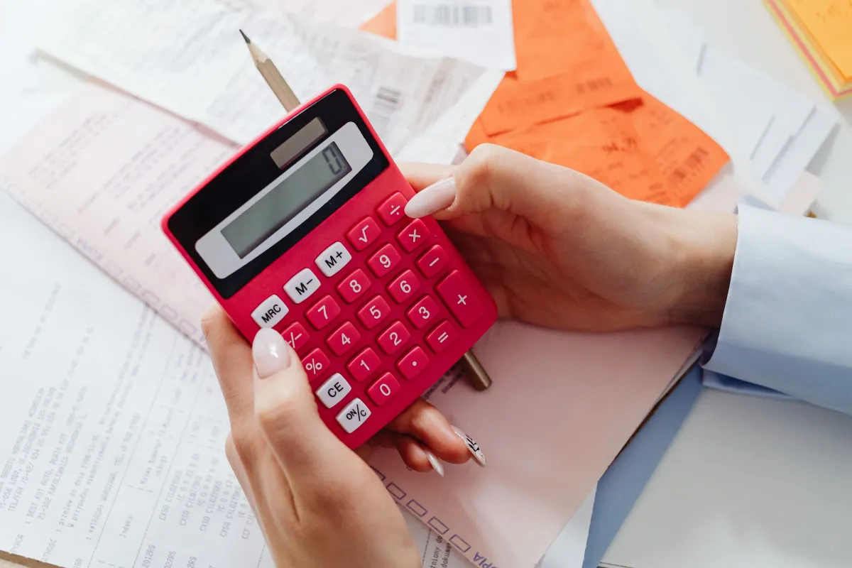 Illustrative stock photo: hands checking figures with a red calculator and receipts