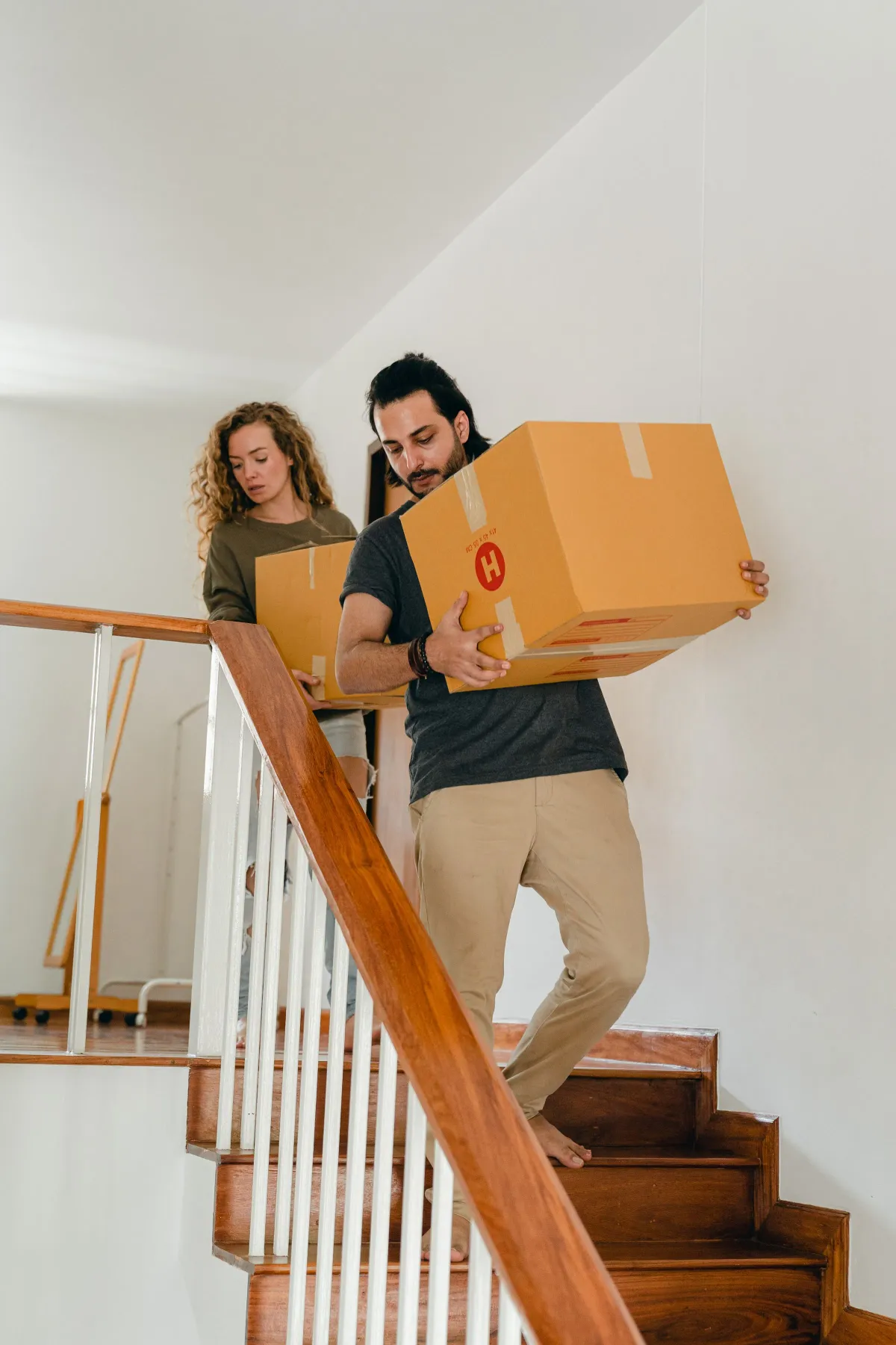 Illustrative stock photo: two people carrying moving boxes up an indoor wooden staircase