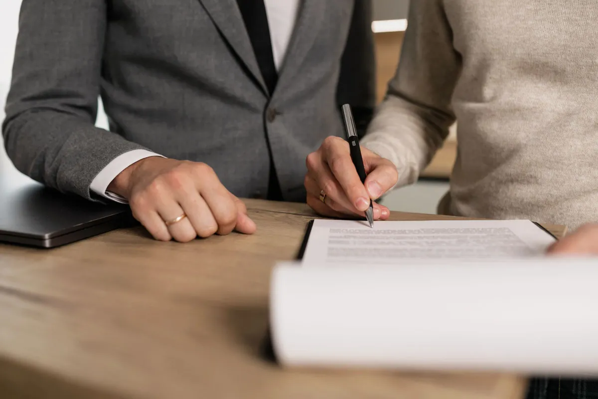 Illustrative stock photo: hands signing documents on a wooden desk