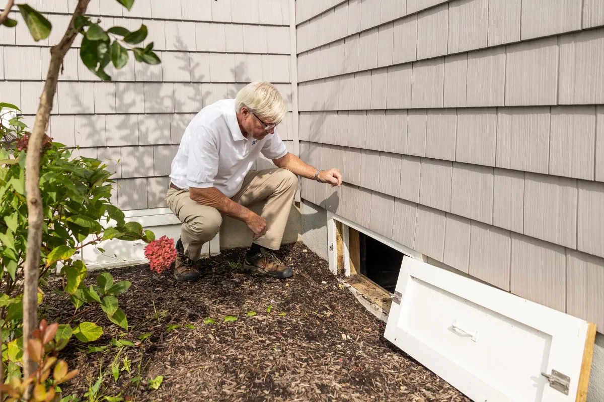 Illustrative stock photo: home inspector examining an exterior crawl-space opening